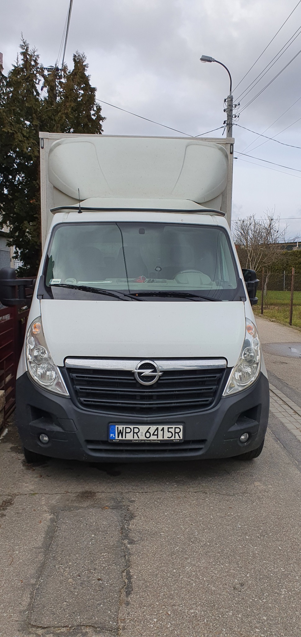 Biały samochód dostawczy Opel Master z zabudową kontenerową, zaparkowany na ulicy, widok z przodu na tablicę rejestracyjną WPR 6415R.