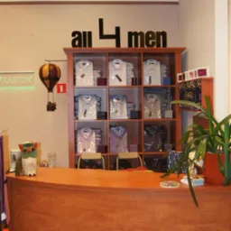 Wnętrze sklepu odzieżowego z drewnianą ladą, regałem wypełnionym zapakowanymi koszulami męskimi, dekoracyjnym balonem na ogrzane powietrze i napisem 'all 4 men' na ścianie.