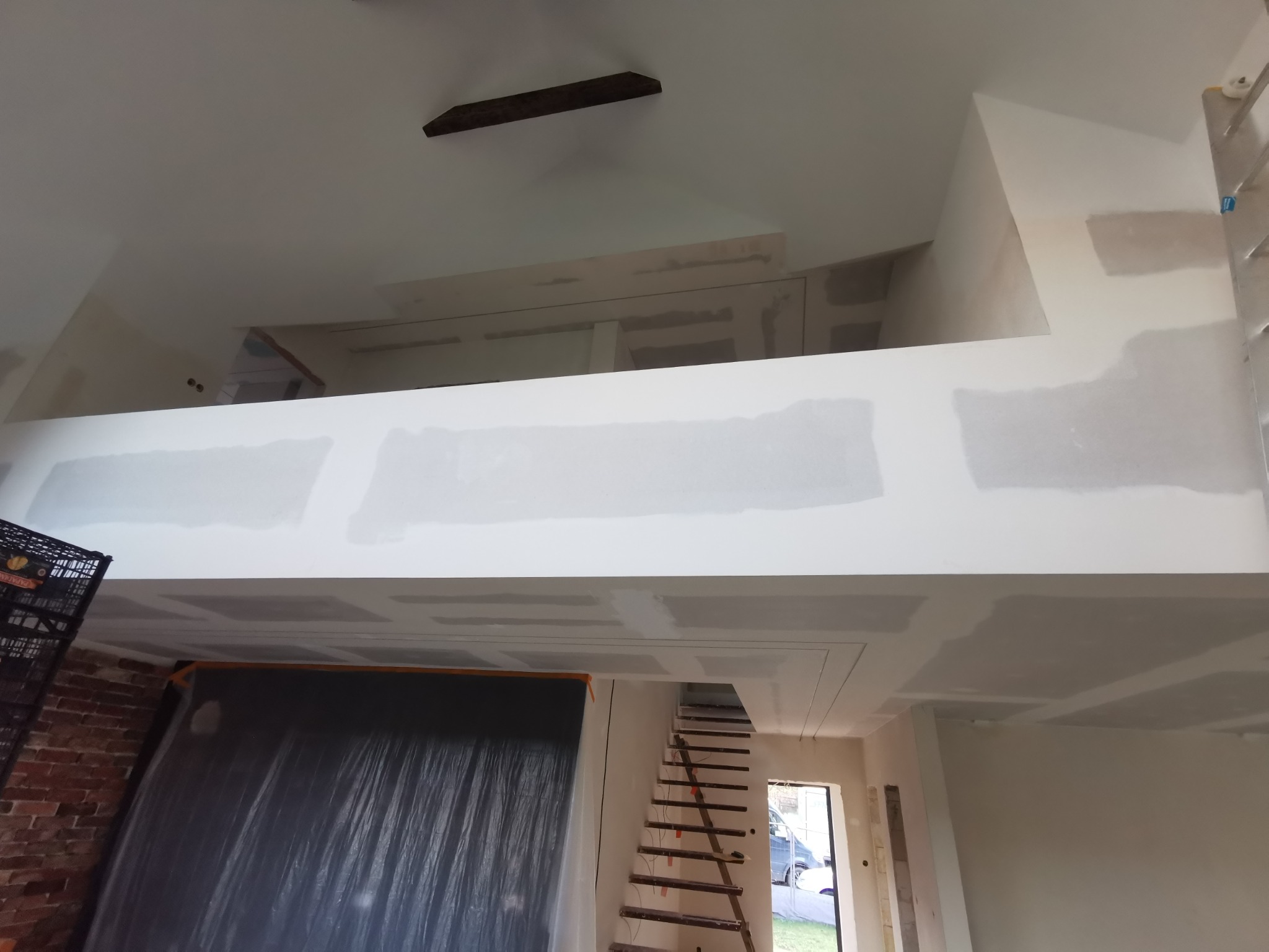 Wnętrze w trakcie prac wykończeniowych: płyty gipsowo-kartonowe na ścianach i suficie, widoczne łączenia wymagające szpachlowania. Schody prowadzą na antresolę.