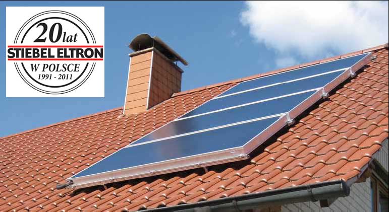 Panele solarne marki Stiebel Eltron zamontowane na dachu z czerwonej dachówki, widoczny komin i logo firmy w lewym górnym rogu.