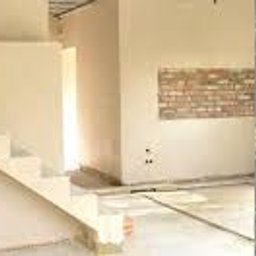 Krzysztof Uchacz-AUTORYTET - Wnętrze w stanie surowym z widocznymi schodami betonowymi, fragmentem ściany z cegły i kolumną z szarego betonu, przygotowane do prac wykończeniowych.