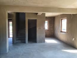 Wnętrze domu w Krakowie w trakcie prac wykończeniowych. Ściany pokryte świeżo nałożonym tynkiem, widoczne surowe ościeżnice okien i drzwi, oraz schody w stanie deweloperskim.