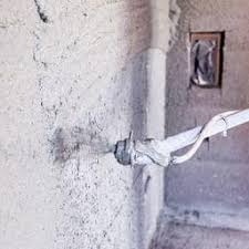 Aplikacja świeżej warstwy zaprawy na ścianie za pomocą dyszy natryskowej, widoczne przewody i puszka elektryczna w tle.