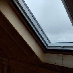MTM DOMY SZKIELETOWE SPÓŁKA Z OGRANICZONĄ ODPOWIEDZIALNOŚCIĄ - Wewnętrzny widok okna dachowego z drewnianą ramą, zamontowanego w konstrukcji dachu o drewnianym wykończeniu, z widokiem na pochmurne niebo.