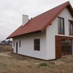 Nowoczesny dom jednorodzinny z czerwoną dachówką, białymi ścianami i drewnianymi akcentami. Widok z zewnątrz, na tle pochmurnego nieba i krajobrazu.