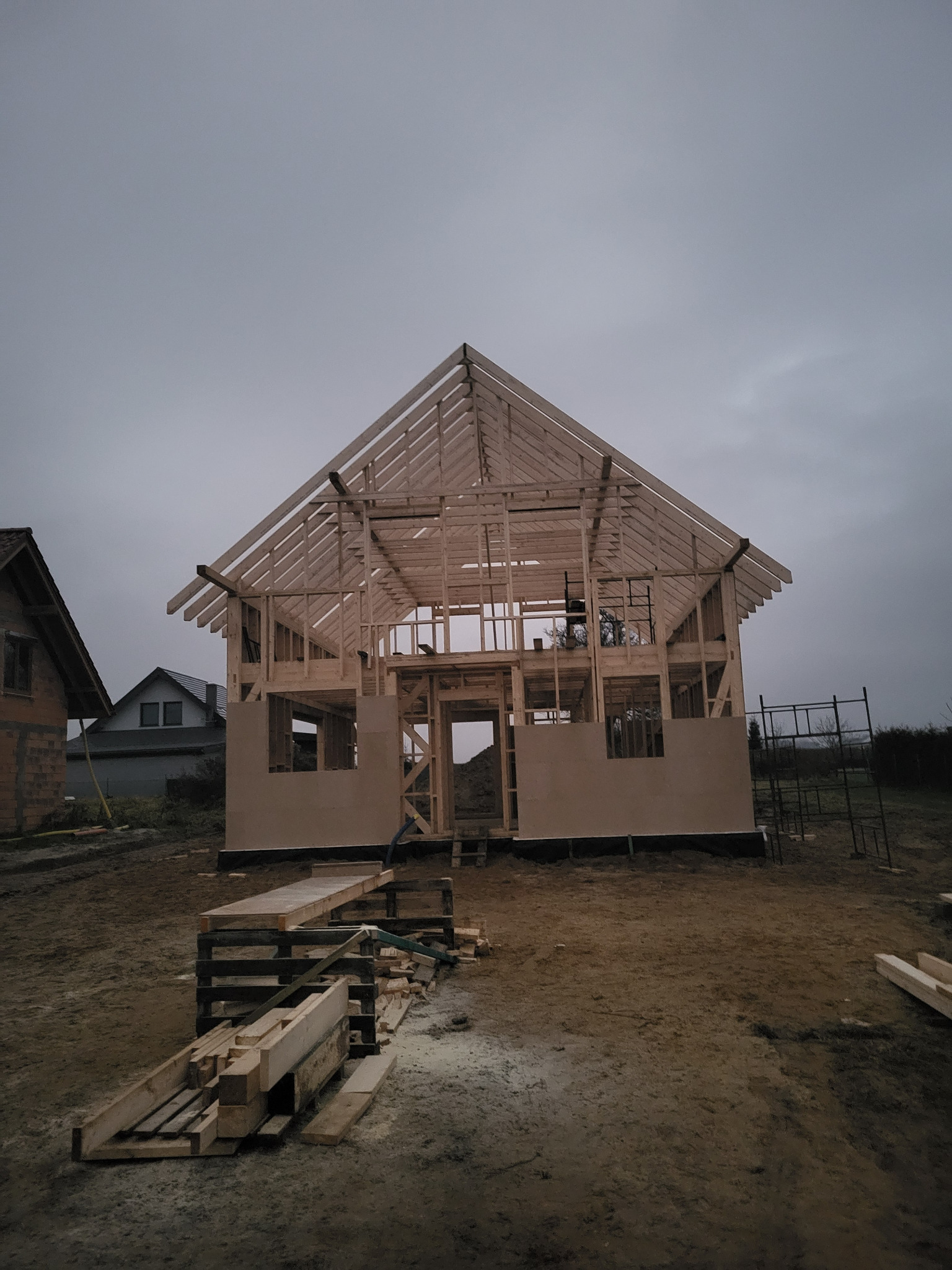 Konstrukcja domu w technologii szkieletowej w trakcie budowy, widok z zewnątrz. Na pierwszym planie drewniane elementy konstrukcyjne.