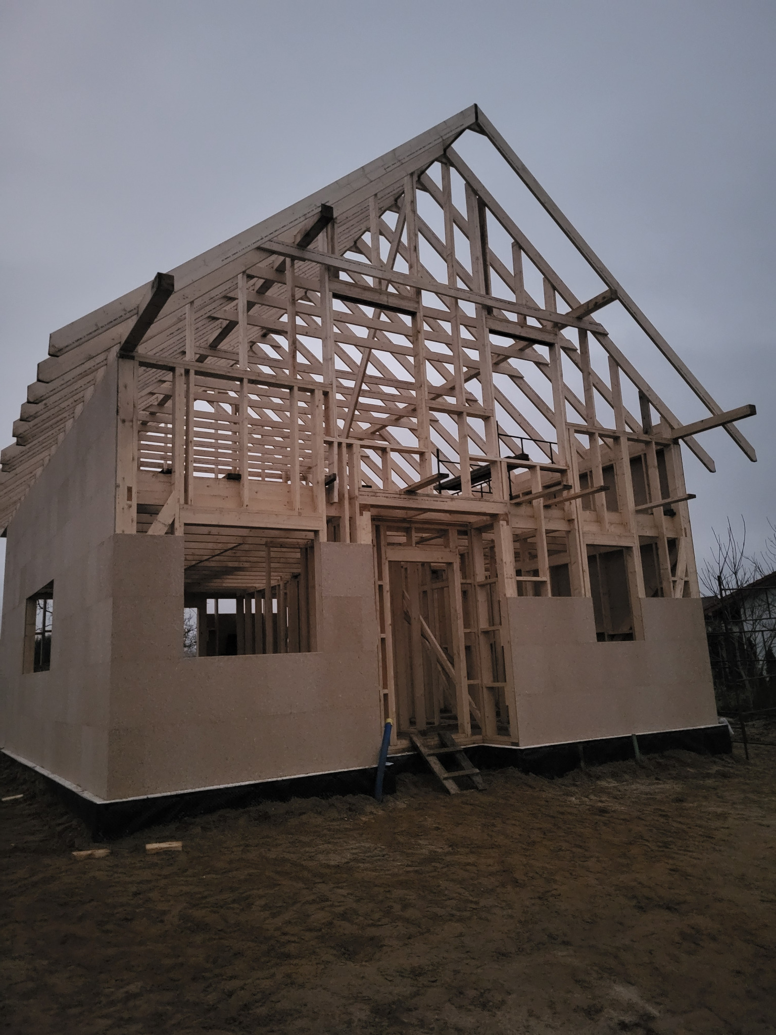 Konstrukcja domu w technologii szkieletowej w trakcie budowy, widoczne drewniane elementy ścian i dachu, płyty OSB. Ujęcie z dołu w pochmurny dzień.