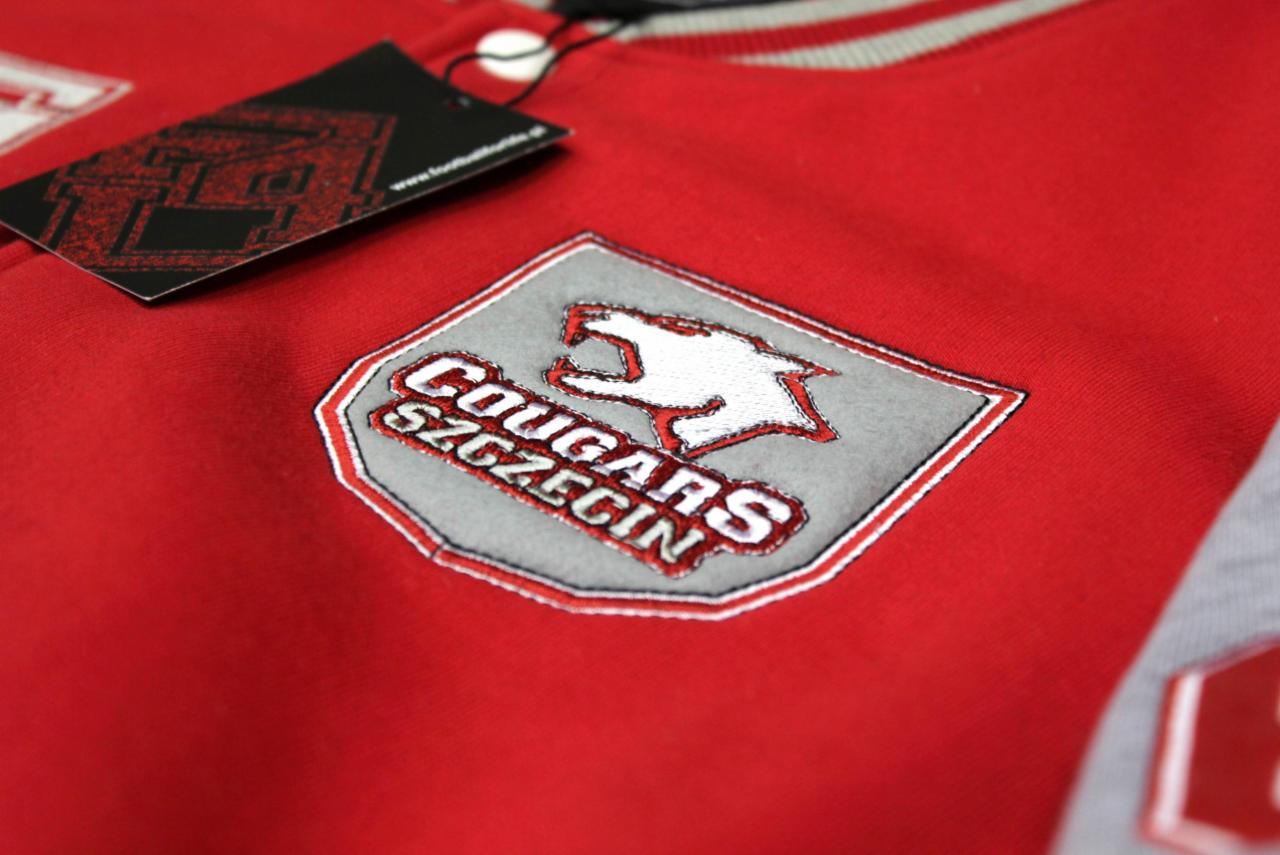 Czerwona kurtka bejsbolówka z naszywką 'Cougars Szczecin' i metką, widok z bliska na detal.