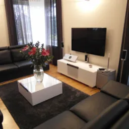 Nowoczesny salon z czarną skórzaną sofą, białym stolikiem kawowym z kwiatami, białą szafką RTV i wiszącym telewizorem.