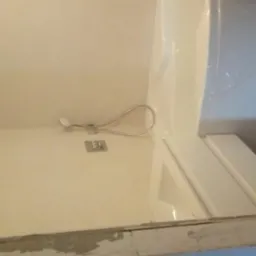 Biała kabina prysznicowa z zamontowaną deszczownicą i słuchawką prysznicową, widoczne płytki z wzorem w tle.