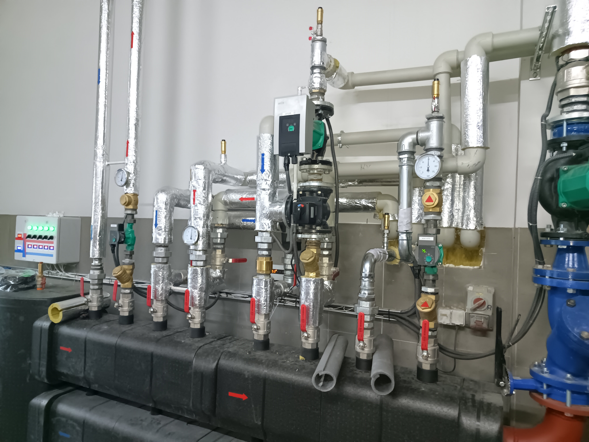 Szczegółowe ujęcie instalacji hydraulicznej z licznymi rurami, zaworami i manometrami. Elementy pokryte izolacją termiczną, widoczne pompy obiegowe i system sterowania.
