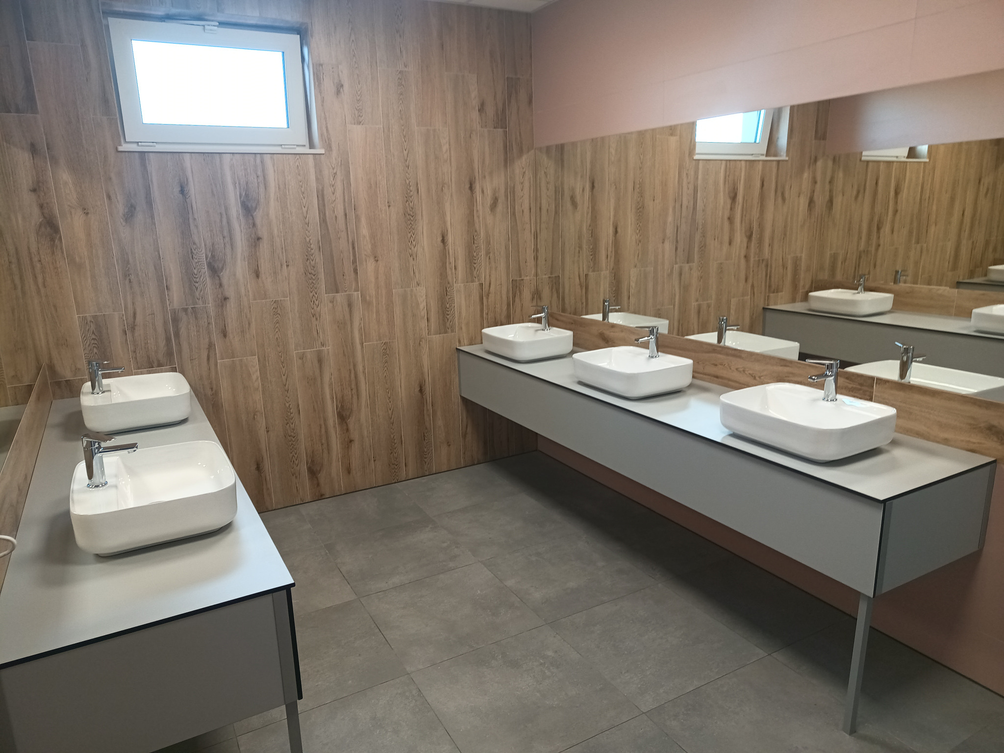 Nowoczesna łazienka z umywalkami nablatowymi i armaturą. Drewnopodobne płytki na ścianach, duże lustro. Minimalistyczny design i jasne wnętrze.