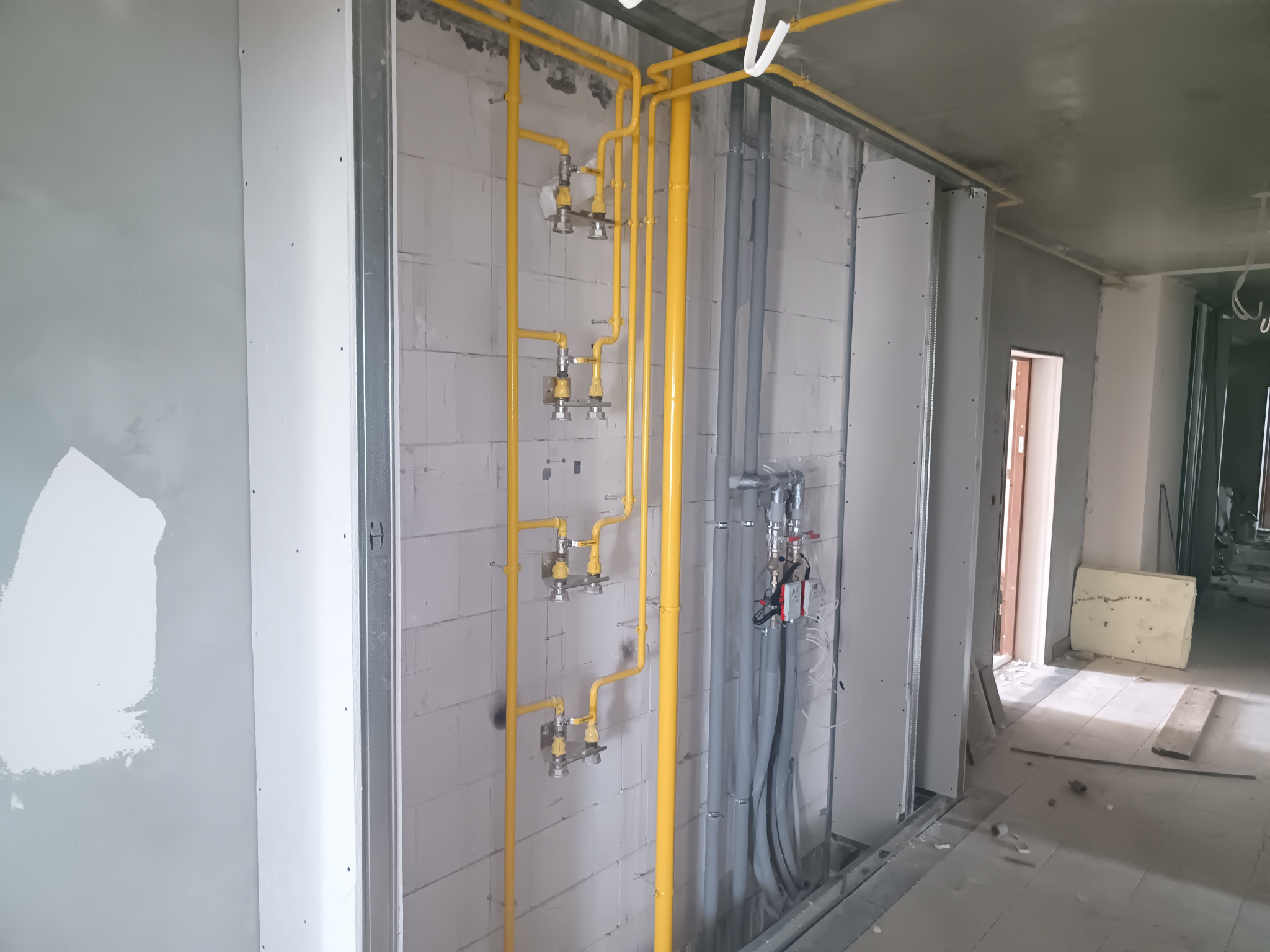 Żółte rury gazowe i szare rury hydrauliczne zamontowane na ścianie z białych bloczków w surowym wnętrzu budynku w trakcie prac instalacyjnych.
