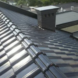 Błyszczący, czarny dach ceramiczny z kominem z cegły klinkierowej w słoneczny dzień.