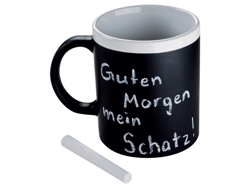 Czarny kubek z powierzchnią do pisania kredą, z napisem 'Guten Morgen mein Schatz!' napisanym białą kredą, obok leży kawałek kredy.