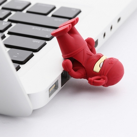 Czerwony pendrive w kształcie ninja wpięty do portu USB białego laptopa, widoczna klawiatura laptopa, białe tło.