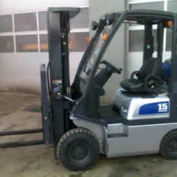 Szaro-niebieski wózek widłowy Nissan PD01A15PQ, widok z boku na tle garażu z bramą segmentową.