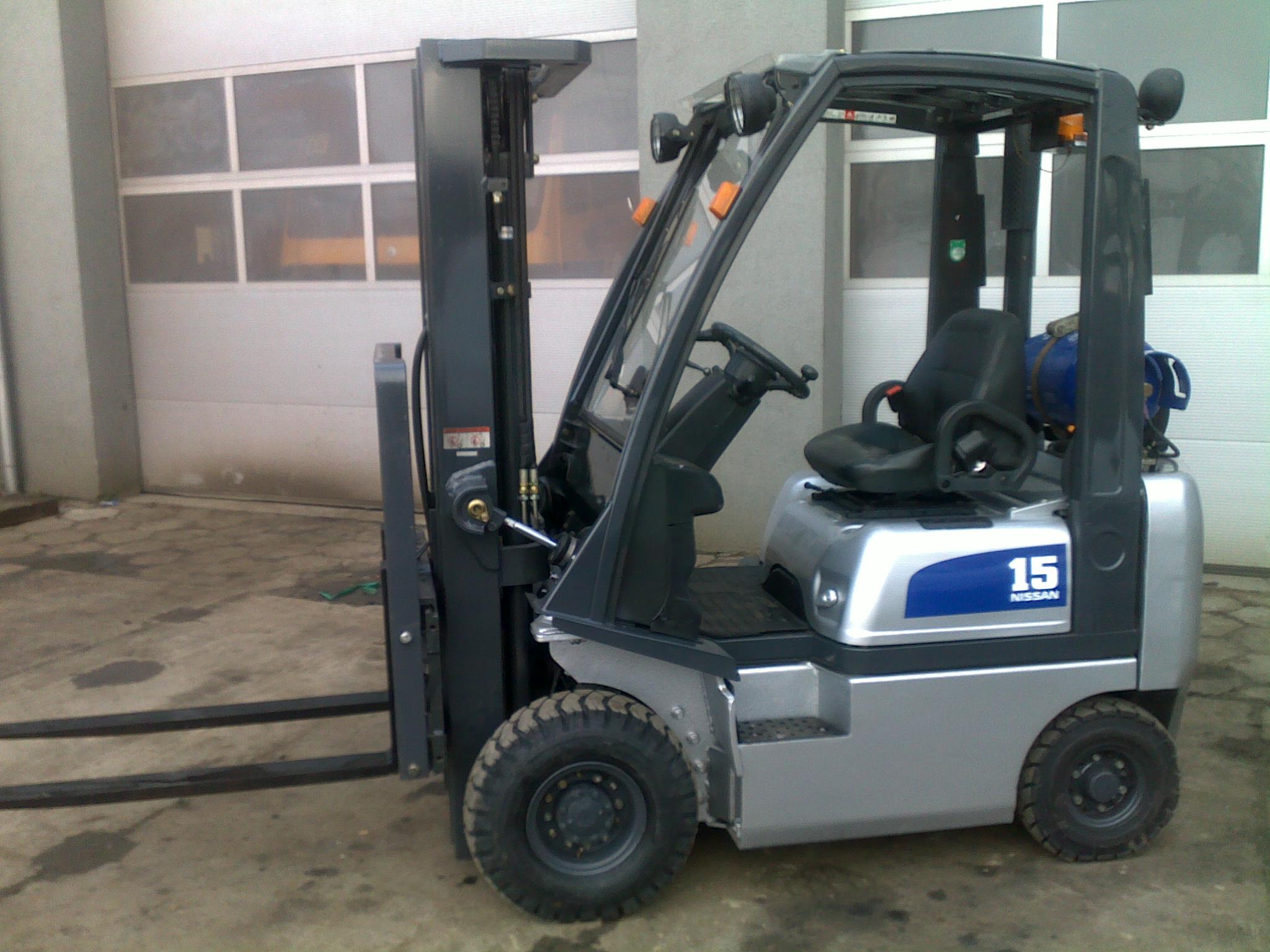 Szaro-niebieski wózek widłowy Nissan PD01A15PQ, widok z boku na tle garażu z bramą segmentową.