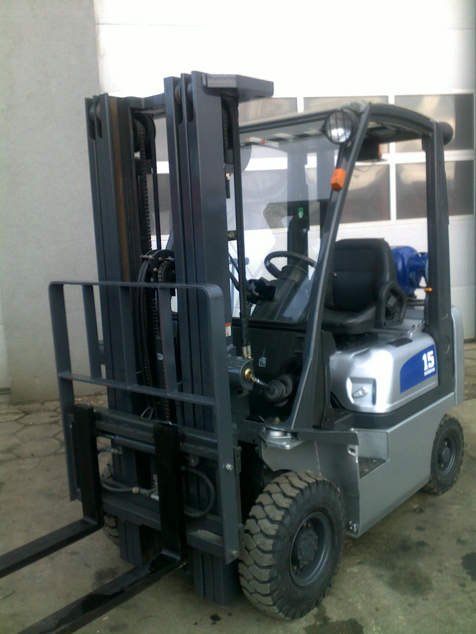 Nowy wózek widłowy Nissan PD01A15PQ, szaro-niebieski z czarnym siedziskiem, stojący przed zamkniętą bramą garażową.