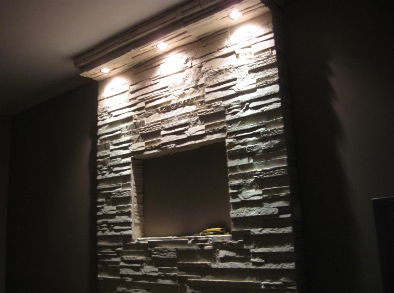 Ściana z dekoracyjnej cegły z podświetleniem LED i wnęką, na półce wewnątrz wnęki leży nóż tapicerski.