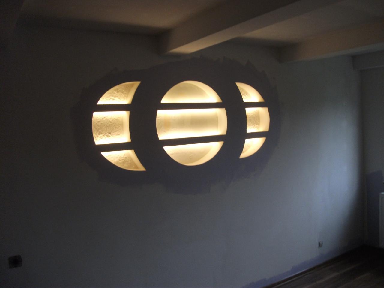 Nietypowa wnęka ścienna z oświetleniem LED w kształcie trzech połączonych okręgów, w trakcie szpachlowania i wygładzania. Widoczne nierówności na ścianie wokół wnęki.