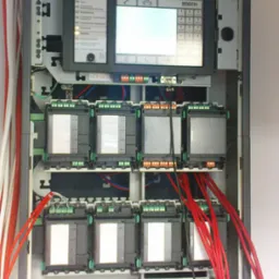 Panel sterowania systemem alarmowym Bosch z wyświetlaczem, klawiaturą i modułami z licznymi połączeniami kablowymi w kolorze czerwonym i białym, zainstalowany w szafie rack.