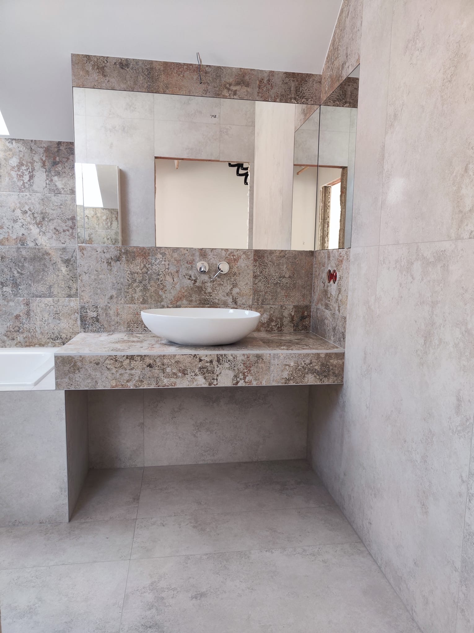 Wykończona łazienka z umywalką nablatową, lustrem wklejonym w płytki i baterią podtynkową, w neutralnej kolorystyce szarości i beżu.