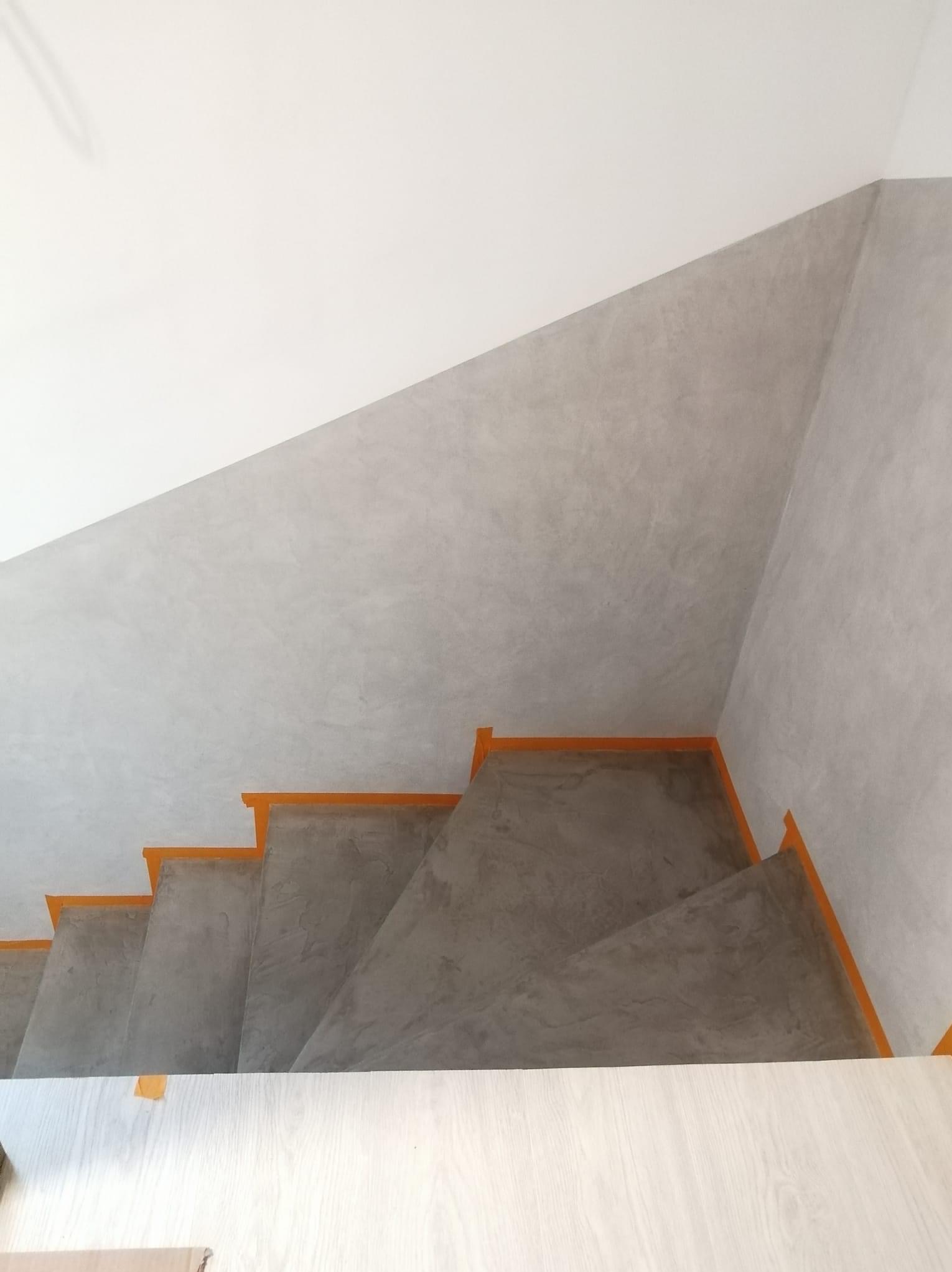 Schody betonowe zabezpieczone pomarańczową taśmą malarską, ściany pokryte szarą gładzią, widok z góry.