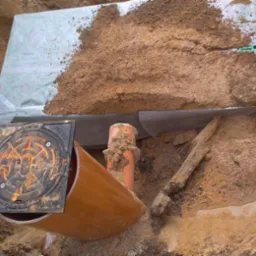 Wykonana instalacja wodno-kanalizacyjna w wykopie, z widoczną rurą, studzienką rewizyjną i zabezpieczeniem. Etap prac ziemnych.