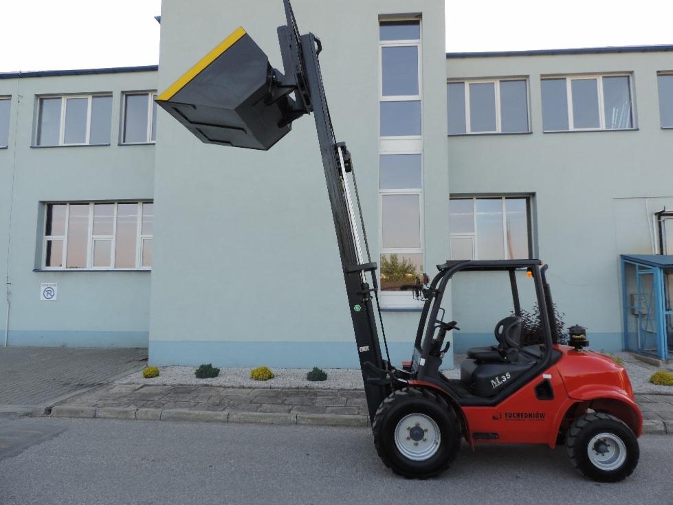 Czerwony wózek widłowy M.35 Suchedniów z zamontowanym pojemnikiem na wysięgniku, stojący na tle budynku z oknami. Widok z boku, oświetlenie dzienne.