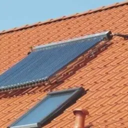 Kolektory słoneczne rurowe zamontowane na skośnym dachu z czerwonej dachówki ceramicznej, widoczne mocowania i rury doprowadzające.