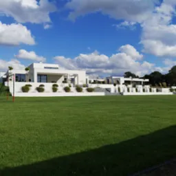 Rozległy, idealnie utrzymany trawnik przed nowoczesnym, białym domem z płaskim dachem, na tle błękitnego nieba z białymi obłokami. W tle widoczna zieleń drzew i krzewów. Na trawniku stoi bramka...