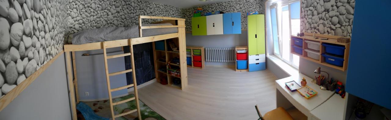 Pokój dziecięcy z drewnianym łóżkiem na antresoli z drabinką, biurkiem przy oknie, szafkami w kolorach zielonym, niebieskim i białym oraz tapetą imitującą kamienie.